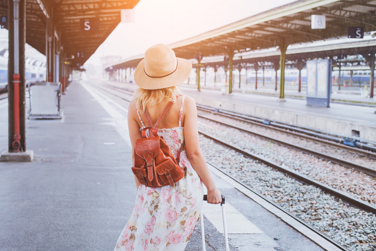 joven con sombrero y maleta en el andén de la estación